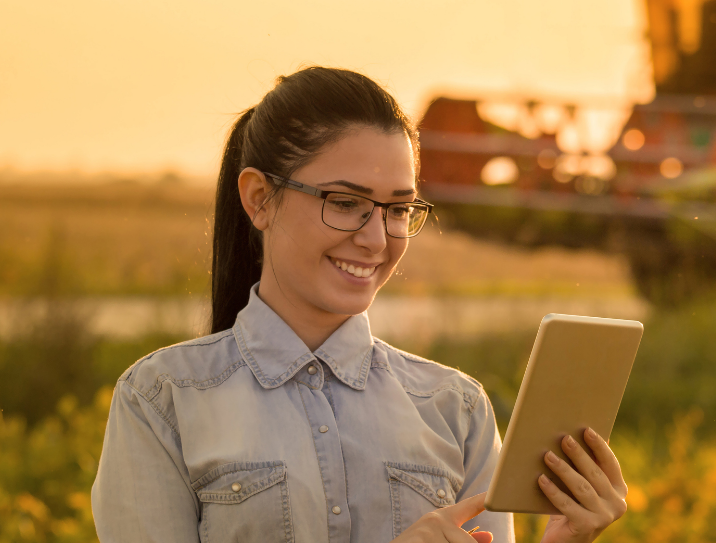 mulher morena usando óculos de grau sorri para tablet no campo